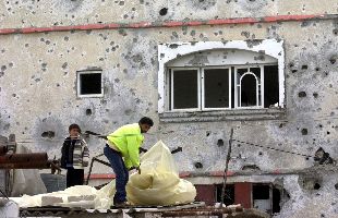 Un palestino cubre el techo de su vivienda con plásticos, frente a un muro dañado por proyectiles, ayer, al sur de Gaza.