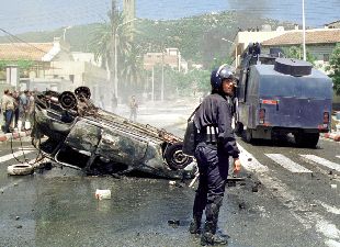 Un policía antidisturbios, junto a un coche quemado el domingo en una calle de Tizi Uzu, la capital bereber de Argelia.