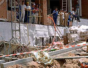 Compañeros de los dos obreros fallecidos contemplaban ayer el cadáver, cubierto, de uno de ellos sobre los escombros del andamio siniestrado.