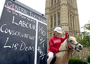 Un jinete con una máscara de Tony Blair, junto a una lista de apuestas sobre las elecciones, ayer en Londres.