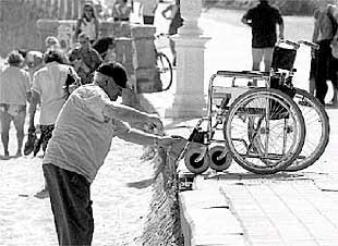 Un anciano intenta acceder a su silla de ruedas desde la playa de Ondarreta, en San Sebastián.
