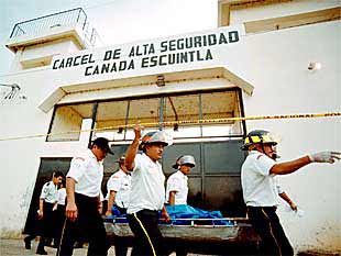 Equipos de rescate sacan de la prisión donde se produjo la fuga el cadáver de un policía asesinado.