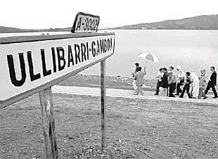 Un grupo de paseantes, a orillas del embalse, pasa delante de una antigua señalización del pueblo.
