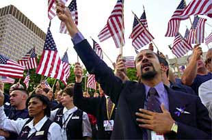Un representante de American Airlines sostiene una bandera en alto con la mano en el corazón junto a otros norteamericanos en una plegaria en Boston.
