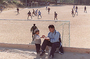 Un jugador de la Liga de fútbol de ecuatorianos atiende a un niño mientras sus compañeros disputan un partido.