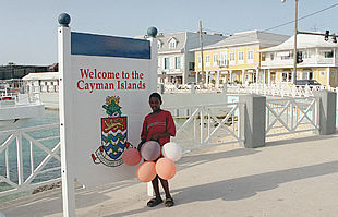 Un niño, junto a un cartel de bienvenida a Georgetown, capital del paraíso fiscal de Gran Caimán.