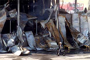 Un bombero camina junto a los restos calcinados de la fábrica de Campocarne en Arganda.