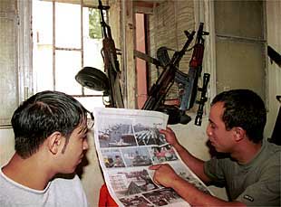 Dos jóvenes palestinos provistos de fusiles leen un periódico en un campo de refugiados del sur de Líbano.