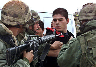 Un militar israelí apunta con su fusil de asalto M-16 a un joven palestino en un control de carreteras entre Ramala y Jerusalén.