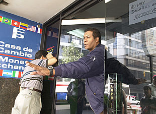 Un empleado de una casa de cambio informa a los clientes de que no vende dólares por no disponer de efectivo.