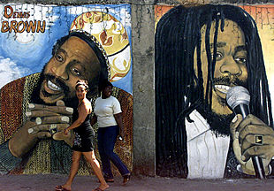 Dos jamaicanas pasan delante de un mural que representa a los músicos de  reggae  Denis Brown y Bob Marley en la capital, Kingston, adonde llegaron ayer Isabel II de Inglaterra y su esposo.