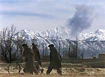 Varios afganos, en el pueblo de Surmad, con una columna de humo provocada por los bombardeos al fondo.