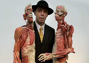 Gunther von Hagen posa entre dos cuerpos revestidos de material plástico que se exhiben en  Mundos corporales. 