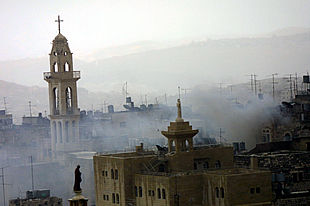 El humo provocado por los enfrentamientos ante la basílica de la Natividad se eleva sobre el campanario (izquierda).