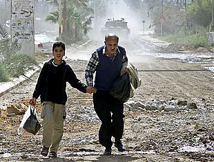 Un niño y un hombre palestinos  corren por una calle de Yenín, en Cisjordania, ante un tanque israelí.