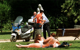 Dos muchachas toman el sol en el parque de la Ciutadella, mientras la policía cachea a un joven.