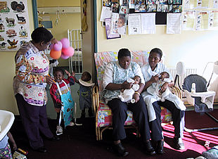 Stella, a la izquierda, juega con unos globos; a la derecha, dos voluntarias dan el biberón a Dawood y Boituneso en el hospicio de Cotlands.