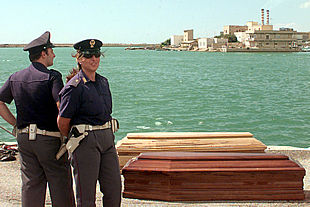 Dos policías italianos permanecen junto a los ataúdes de varios de los inmigrantes fallecidos en el naufragio. PLANO GENERAL - ESCENA