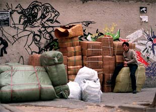 Un hombre, sentado en un fardo junto al resto de mercancía de un comercio al por mayor apilada en una calle de Lavapiés.