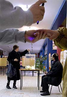 Un vocal de mesa controla a un votante marcado con tinta invisible.