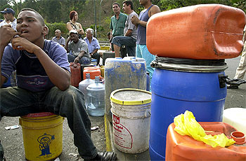 Un joven, rodeado de bidones de gasolina, espera junto a un surtidor de gasolina en Caracas.
