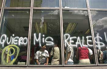 Un grupo de personas espera en un banco de Caracas, tras una pintada que exige poder retirar el dinero.