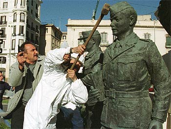 Un policía, con la pistola en la mano, intenta impedir el destrozo de un monumento militar de Alicante.