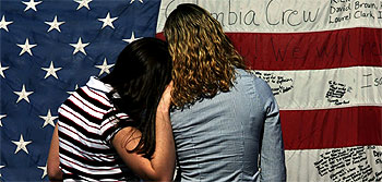Dos adolescentes leen los mensajes escritos en una bandera por los asistentes a la ceremonia de homenaje a la tripulación del  Columbia  celebrada el martes en Houston.