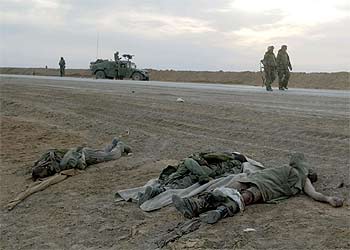 'Marines' estadounidenses caminan por una carretera del sur de Irak junto a los cadáveres de tres soldados iraquíes.