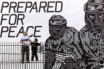 Un hombre y un niño, delante de una inmensa pintada mural del IRA con la leyenda 