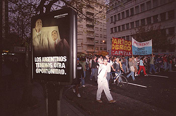 Una manifestación obrera en Buenos Aires pasa ante un cartel electoral de Menem.