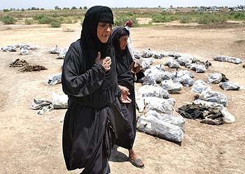 Varios iraquíes, ayer, entre las bolsas de plástico que contienen algunos de los miles de restos humanos encontrados en una fosa común en Irak.