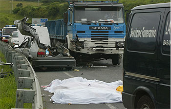 El turismo siniestrado en Abanto, junto al camión con el que colisionó y los cadáveres de los fallecidos cubiertos con sábanas.