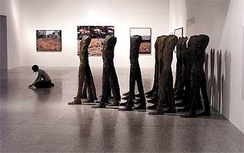 Una joven toma notas en la muestra junto a  Caminando  (1998-1999), conjunto escultórico de la polaca Magdalena Abakanowicz. Al fondo, tres fotografías del norteamericano Spencer Tunick.