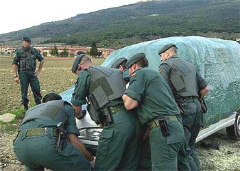 Guardias civiles cubren la furgoneta desde la que ayer fue lanzada una granada contra un cuartel, al fondo.