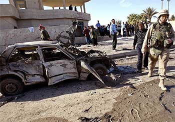 Un oficial estadounidense pasa junto a un vehículo destrozado por la explosión registrada ayer en la localidad de Jalidiya.