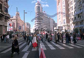 Decenas de peatones cruzan la Gran Vía, a la altura de la plaza del Callao, en el último domingo navideño de cortes de tráfico.