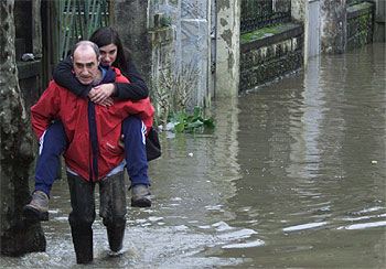 Un hombre con botas de agua traslada a una joven por la inundada carretera GI-131, a su paso  el barrio donostiarra de Martutene.