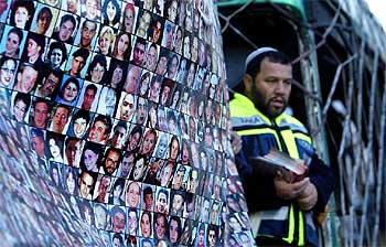Un israelí posa delante de un autobús atacado por un suicida palestino y las fotografías de víctimas de la Intifada, en la vista de ayer en La Haya.