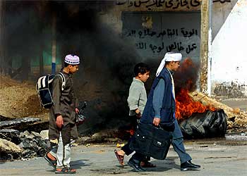 Estudiantes palestinos pasan por delante de un neumático calcinado después de un ataque del Ejercitó israelí ayer en Gaza.