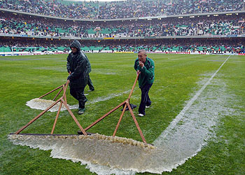 Operarios del Betis intentan retirar el agua del césped.
