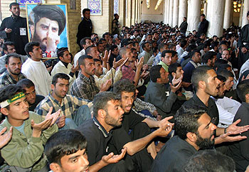 Varios chiíes rezan en una mezquita de Nayaf enarbolando un cartel con el rostro de Múqtada al Sáder.