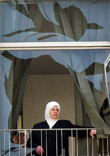 Una mujer mira a través de los cristales rotos de un edificio de Damasco.