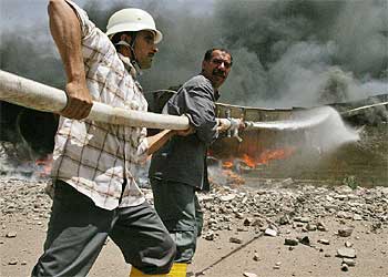 Dos bomberos iraquíes luchan para extinguir un incendio en un depósito de combustible tras un ataque con morteros en Abu Ghraib.