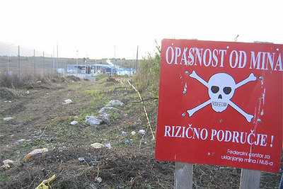 Un cartel oficial avisa del peligro de minas en un descampado cerca de Bihac, en el noroeste de Bosnia-Herzegovina. Se conocen 18.600 lugares como éste. Al fondo, el puesto de la frontera con Croacia.