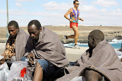Tres de los inmigrantes llegados en patera a Fuerteventura. Al fondo, un hombre hace  footing. 