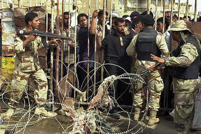 Miembros de la Guardia Nacional iraquí controlan el acceso a un estadio de Bagdad atacado ayer y al que milicianos chiíes acuden a entregar armas.