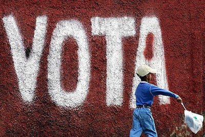 Un niño pasa por delante de una pintada que invita a participar en las elecciones en una calle de Caracas.