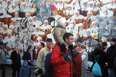 Turistas en el carnaval de Binche, en Bélgica, con los  Gilles,  los personajes característicos de la celebración, representados en la pared.