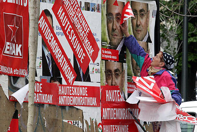 Un mujer arranca los letreros con el lema  Elecciones antidemocráticas  pegados sobre carteles de propaganda electoral en las calles de Bilbao.